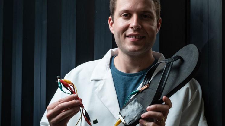Rice University postdoctoral researcher Michael Stanford holds a flip-flop with a triboelectric nanogenerator, based on laser-induced graphene, attached to the heel.